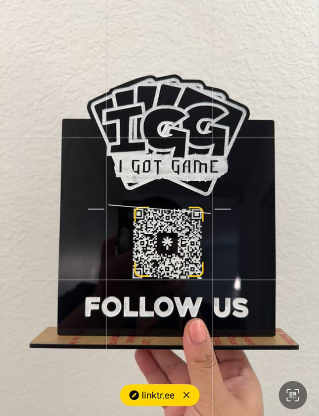 Hand holding a sign with 'I Got Game' branding and QR code on a light background