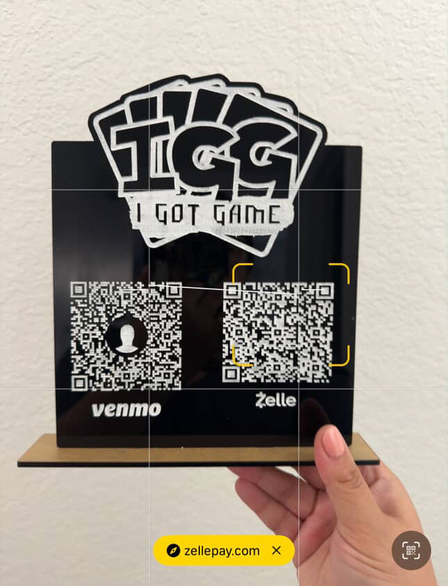 Hand holding a card with 'I Got Game' branding and QR code on a light-colored wall background.